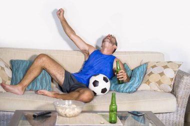 genç çekici adam mutlu ve heyecanlı izlerken futbol maçı televizyonda zafer hedef deli ve spastik bira patlamış mısır ve futbol topu ile kutluyor 
