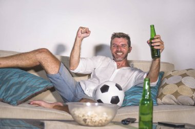 genç çekici adam mutlu ve heyecanlı izlerken futbol maçı televizyonda zafer hedef deli ve spastik bira patlamış mısır ve futbol topu ile kutluyor 