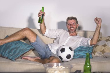 genç çekici adam mutlu ve heyecanlı izlerken futbol maçı televizyonda zafer hedef deli ve spastik bira patlamış mısır ve futbol topu ile kutluyor 
