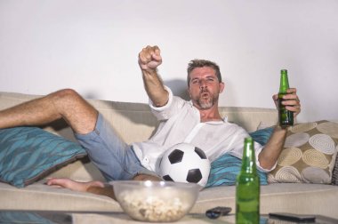 genç çekici adam mutlu ve heyecanlı izlerken futbol maçı televizyonda zafer hedef deli ve spastik bira patlamış mısır ve futbol topu ile kutluyor 