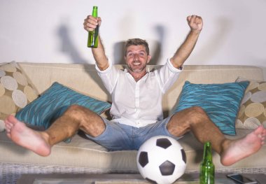 genç çekici adam mutlu ve heyecanlı izlerken futbol maçı televizyonda zafer hedef deli ve spastik bira patlamış mısır ve futbol topu ile kutluyor 