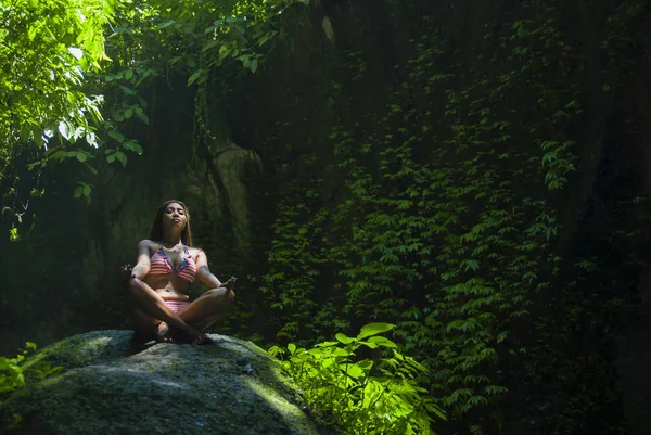 Jovem bela mulher asiática praticando Yoga posando sentado em posição de lótus meditando sobre uma pedra em uma paisagem natural deslumbrante cheia de vegetação — Fotografia de Stock