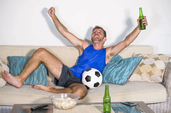 genç çekici adam mutlu ve heyecanlı izlerken futbol maçı televizyonda zafer hedef deli ve spastik bira patlamış mısır ve futbol topu ile kutluyor 