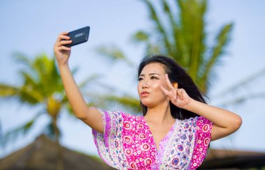 mutlu güzel ve muhteşem Asyalı Çinli kadın kendi kendine portre selfie cep telefonu ile tatil tropikal Resort'ta fotoğrafta glamour elbiseli