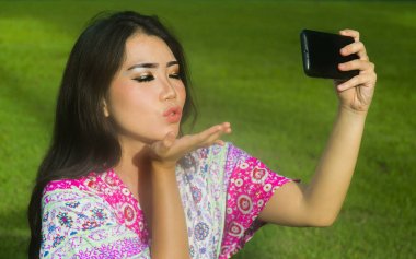 açık havada yeşil çim parkın poz bir öpücük atma cep telefonu kamera ile selfie pic alarak genç mutlu ve güzel Asyalı Çinli kadın 