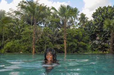 tatil tropikal resort sonsuzluk havuzunda güzel orman peyzaj palmiye ağaçları ile genç çekici mutlu siyah Afrika kökenli Amerikalı kadının