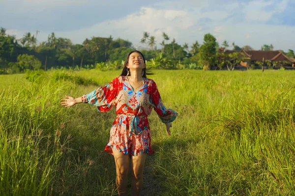 Junge glückliche und verspielte asiatische Chinesin in schönem Kleid, die Spaß hat, Ferien Ausflug auf Gras tropischen Feld lächelnd fröhlich — Stockfoto