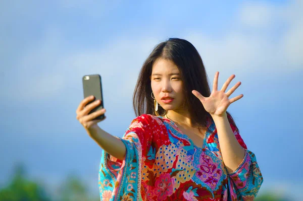 Joven hermosa y feliz asiático chino turista mujer en su 20s con colorido vestido tomando foto selfie con cámara de teléfono móvil en el campo tropical — Foto de Stock
