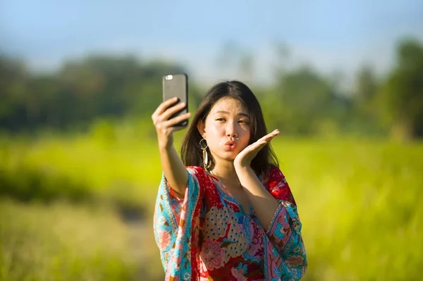 Ung vacker och glad asiatiska kinesiska turist kvinna på hennes 20s med färgglada klänning tar selfie pic med mobiltelefon kamera på tropiska fält — Stockfoto