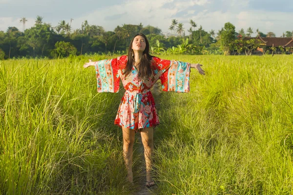 Junge glückliche und verspielte asiatische Chinesin in schönem Kleid, die Spaß hat, Ferien Ausflug auf Gras tropischen Feld lächelnd fröhlich — Stockfoto