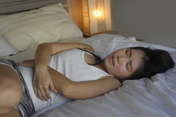 Jonge mooie en vrij Aziatische-Chinese vrouw liggend op bed het gevoel van ziek en onwel buik en maag kramp en menstruatie periode pijn lijden — Stockfoto