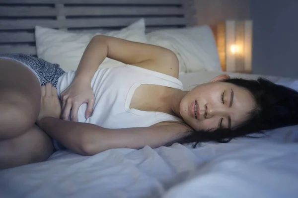 Wanita Cina muda yang cantik dan cantik berbaring di tempat tidur merasa sakit dan menderita perut dan kram perut dan menstruasi periode nyeri — Stok Foto
