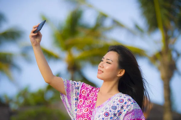 Feliz hermosa y hermosa mujer china asiática en vestido de glamour tomando foto selfie autorretrato con teléfono móvil en vacaciones resort tropical — Foto de Stock