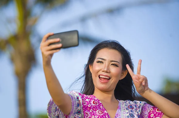 Feliz hermosa y hermosa mujer china asiática en vestido de glamour tomando foto selfie autorretrato con teléfono móvil en vacaciones resort tropical — Foto de Stock