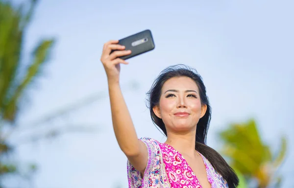 Feliz hermosa y hermosa mujer china asiática en vestido de glamour tomando foto selfie autorretrato con teléfono móvil en vacaciones resort tropical —  Fotos de Stock