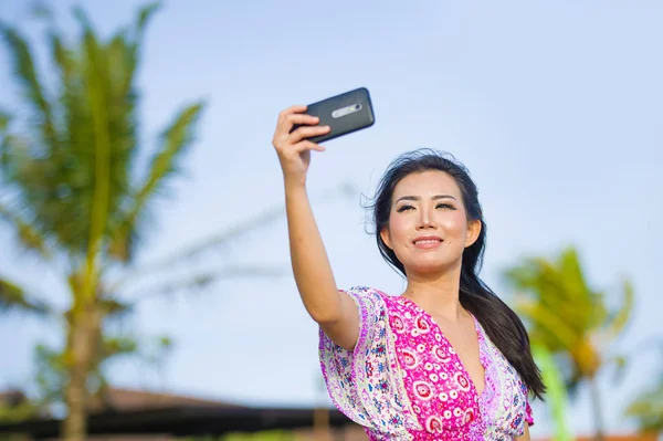 愉快的美丽和华丽的亚洲中国妇女在魅力礼服采取自画像自拍照片与移动电话在假日热带度假胜地 — 图库照片