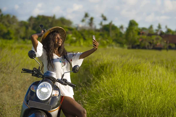 Young attractive black afro American tourist woman in Asian traditional hat riding motorbike taking selfie photo with mobile phone smiling happy — Stock Photo, Image