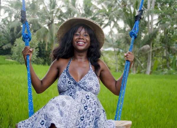 Fiatal gyönyörű turista afro-amerikai fekete nő lovaglás swing élvezi, és mosolygós boldog visel hagyományos ázsiai kalapot trópusi dzsungelben és a rizs mező — Stock Fotó