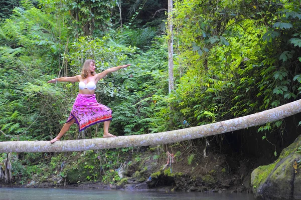 Atraente mulher caucasiana dos anos 30 em equilíbrio posição de ioga no tronco fino sobre o rio em relaxamento e meditação em uma bela paisagem da selva da floresta tropical — Fotografia de Stock