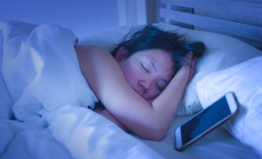 Genç tatlı ve güzel Asyalı Çinli kadın 20'li yaşlarda ya da cep telefonu internet sosyal medya bağımlılığı yanındaki yatakta uyuyan 30s portre kadar kapatın