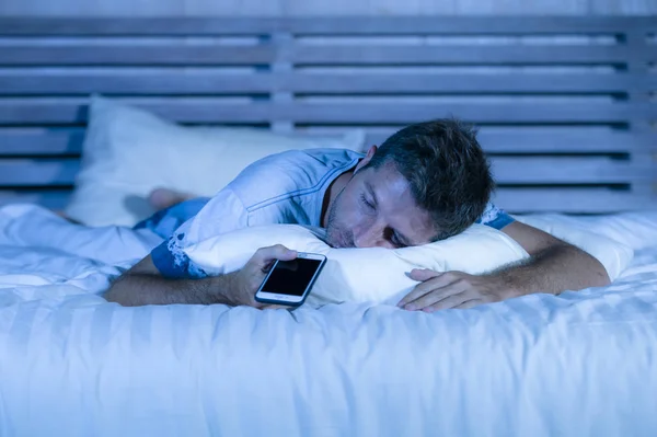 Homem cansado atraente na cama adormecer enquanto usa o telefone celular ainda segurando o celular em sua mão enquanto dorme na internet e vício em mídia social — Fotografia de Stock