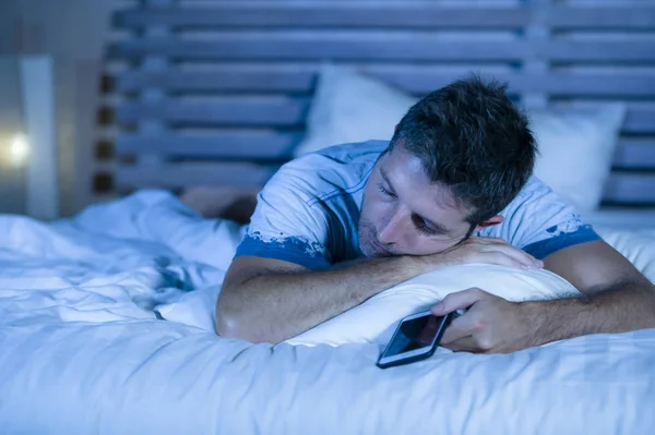 Привлекательный уставший мужчина в постели засыпает во время использования мобильного телефона все еще держа сотовый телефон в руке во время сна в Интернете и в социальных сетях наркомании — стоковое фото