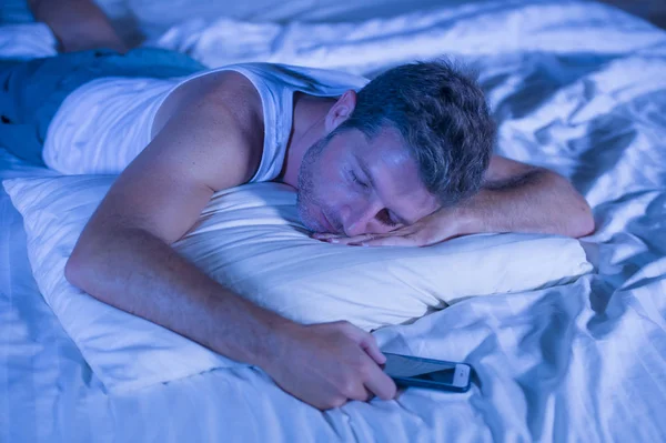 Attraente uomo stanco a letto addormentarsi mentre si utilizza il telefono cellulare ancora tenendo il cellulare in mano mentre dorme in internet e dipendenza dai social media — Foto Stock