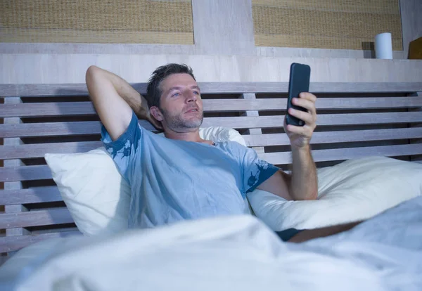 Giovane uomo attraente e felice sdraiato sul letto utilizzando internet cellulare sorridente invio di testo nei social media e dipendenza dalla comunicazione cellulare — Foto Stock