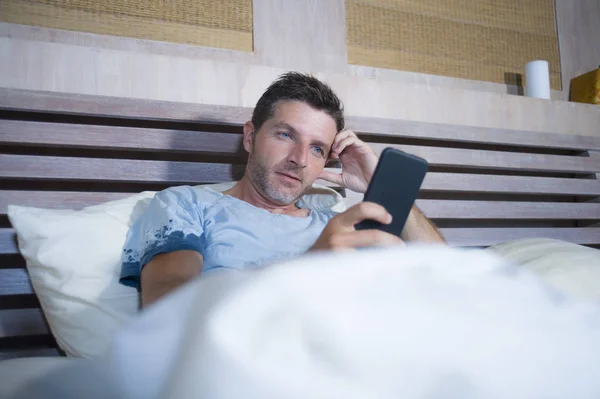 Giovane uomo attraente e felice sdraiato sul letto utilizzando internet cellulare sorridente invio di testo nei social media e dipendenza dalla comunicazione cellulare — Foto Stock