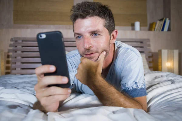 Giovane uomo attraente e felice sdraiato sul letto utilizzando internet cellulare sorridente invio di testo nei social media e dipendenza dalla comunicazione cellulare — Foto Stock