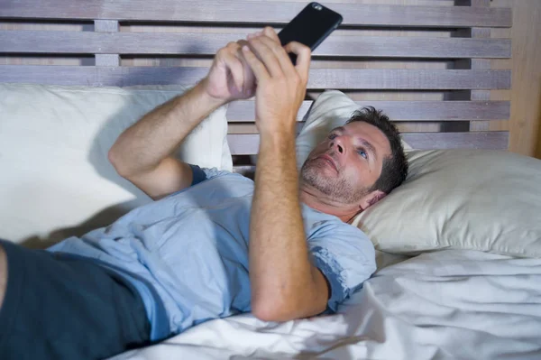 Giovane uomo attraente e felice sdraiato sul letto utilizzando internet cellulare sorridente invio di testo nei social media e dipendenza dalla comunicazione cellulare — Foto Stock