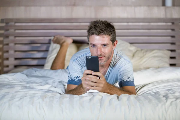 Giovane uomo attraente e felice sdraiato sul letto utilizzando internet cellulare sorridente invio di testo nei social media e dipendenza dalla comunicazione cellulare — Foto Stock