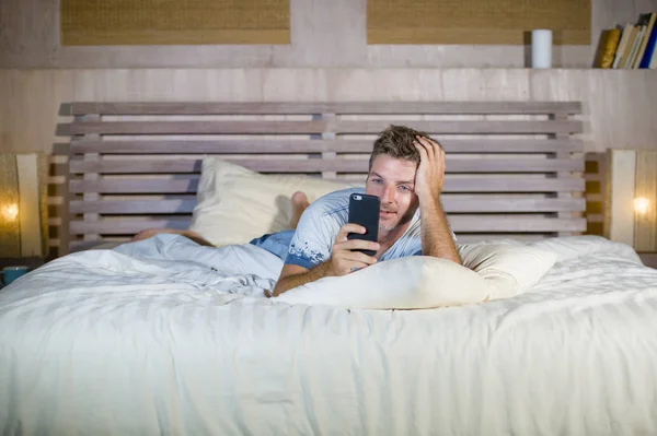 Молодой привлекательный и счастливый мужчина лежит на кровати с помощью интернет-телефона улыбаясь отправка текста в социальных сетях и сотовой связи наркомании — стоковое фото