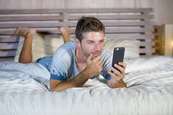 Giovane uomo attraente e felice sdraiato sul letto utilizzando internet cellulare sorridente invio di testo nei social media e dipendenza dalla comunicazione cellulare — Foto Stock