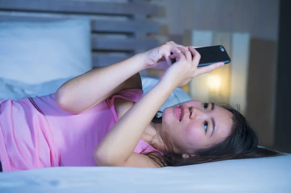Jonge lieve en mooie Aziatische Chinese 20s of 30s vrouw die lacht gelukkig liggend op bed met behulp van internet mobiele telefoon dating of het verzenden van tekst bij nacht — Stockfoto