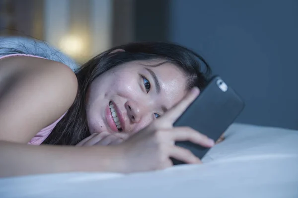 Jeune douce et belle asiatique chinois 20s ou 30s femme souriant heureux couché sur le lit en utilisant Internet téléphone portable sortir ensemble ou envoyer du texte la nuit — Photo