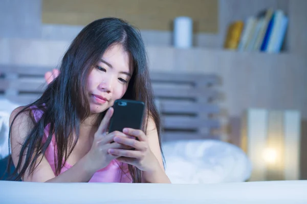 Jeune douce et belle asiatique chinois 20s ou 30s femme souriant heureux couché sur le lit en utilisant Internet téléphone portable sortir ensemble ou envoyer du texte la nuit — Photo