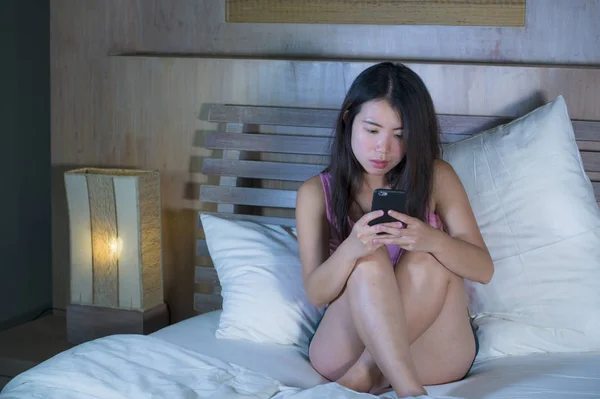 Fiatal édes és gyönyörű ázsiai kínai 20-as vagy 30-as nő mosolyog, boldog ágyon mobiltelefon internet Ismerkedés, vagy küld szöveg éjjel — Stock Fotó