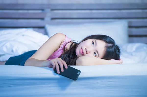 Jeune belle et réfléchie asiatique chinois femme sur son 20s tenant téléphone mobile couché sur le lit la nuit en pensant regarder triste et doux — Photo