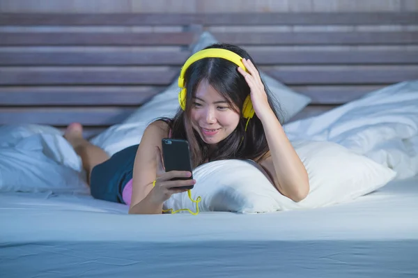 Jeune doux et heureux asiatique chinois 20s femme écouter de la musique chanson avec casque casque et téléphone mobile couché dans le lit détendu tard dans la nuit — Photo