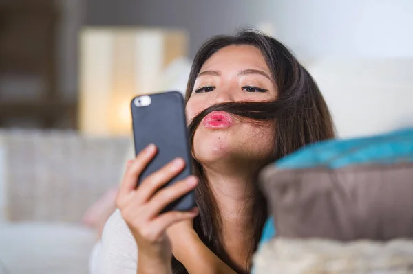 Jeune belle et heureuse asiatique femme chinoise couché sur le canapé à la maison en utilisant Internet sortir ensemble application dans le téléphone mobile prise selfie portrait — Photo