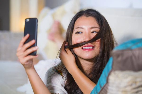 Jeune belle et heureuse asiatique femme chinoise couché sur le canapé à la maison en utilisant Internet sortir ensemble application dans le téléphone mobile prise selfie portrait — Photo