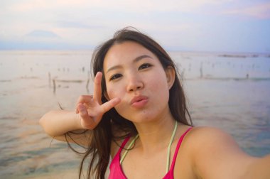 cep telefonu gülümseyen kendi kendine portre selfie alarak genç mutlu ve güzel Asyalı Koreli turist kadın sunset beach adlı eğleniyor