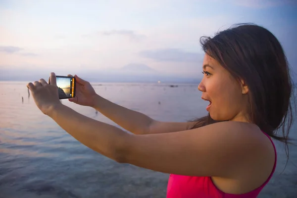 Jovem mulher com câmera de telefone móvel tirando foto da bela praia pôr do sol paisagem e monte Agung vulcão de Bali na Ásia férias viagens — Fotografia de Stock