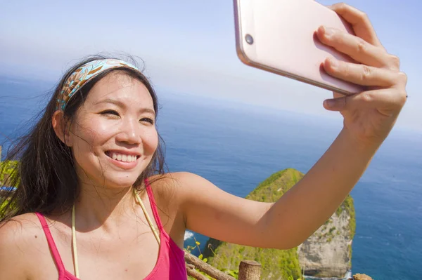 Jovem bonita e feliz asiático coreano turista mulher sorrindo tomando selfie retrato com celular na praia mar penhasco paisagem fundo — Fotografia de Stock