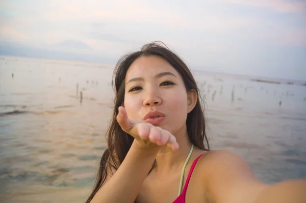 Young happy and beautiful Asian Korean tourist woman taking self portrait selfie with mobile phone smiling having fun at sunset beach — Stock Photo, Image