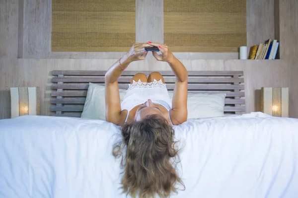 Молодая привлекательная и красивая женщина дома в постели с помощью интернет приложения социальных медиа на мобильном телефоне улыбаясь счастливой — стоковое фото