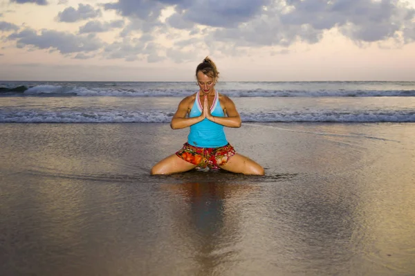 Junge fitte und attraktive Sportlerin im Sonnenuntergang am Strand Yoga-Praxis-Workout sitzend auf nasser Sonne vor dem Meer in Meditation und Entspannungsübungen — Stockfoto