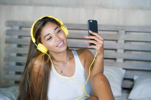 Jovem bela e feliz estudante mulher asiática latina etnia mista ouvir música com fones de ouvido na cama cantando e dançando feliz — Fotografia de Stock