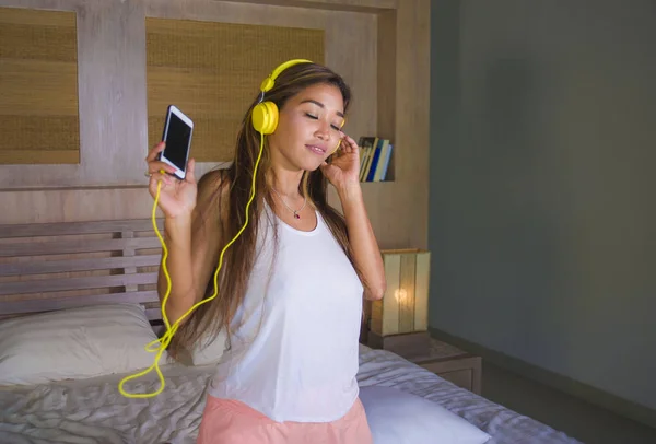 Jovem bela e feliz estudante mulher asiática latina etnia mista ouvir música com fones de ouvido na cama cantando e dançando feliz — Fotografia de Stock